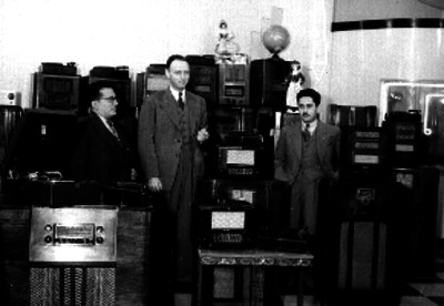 Hombres posando junto a aparatos radiofónicos en una tienda