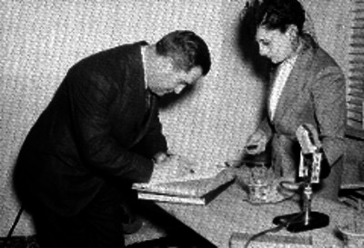 Pereja firmando un documento en una oficina de la Radiodifusora X.E.W.