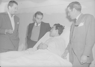 Jorge Aguilar acostado en una cama de hospital conversa con otros hombres