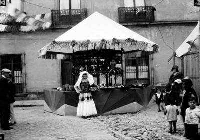 Mujer con traje tehuano junto a un puesto de feria, retrato