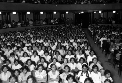 Niñas estudiantes sentadas en un auditorio con palcos, durante una ceremonia escolar
