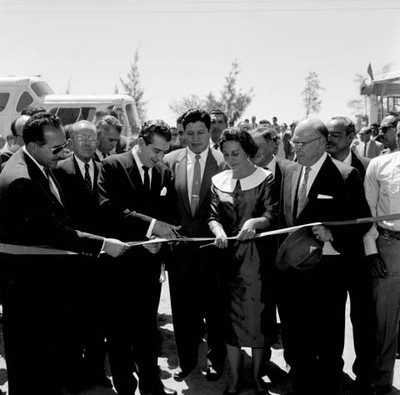 Adolfo López Mateos y Virginia Soto Rodríguez acompañados de funcionarios públicos en el momento de cortar un listón en una inauguración