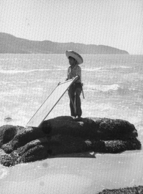 Forillero con un objeto en las manos arriba de una roca cerca del mar