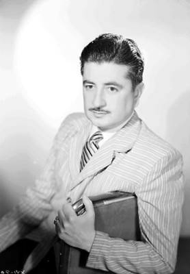 Arturo Corona, actor, porta saco a rayas, sentado en una silla, retrato