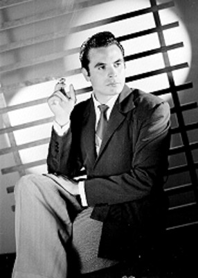 Fernando Casanova, actor, viste de traje y corbata, con cigarrillo encendido en su mano derecha, retrato