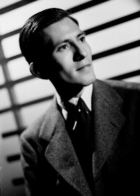 Aldo Cadena, con escenografía de persianas al fondo, viste formal, retrato