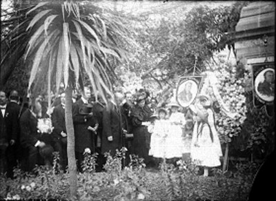 Gente junto a ofrenda floral depositada en un monumento durante las fiestas del centenario