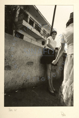 Muchacha recostada en un muro con edificio al fondo
