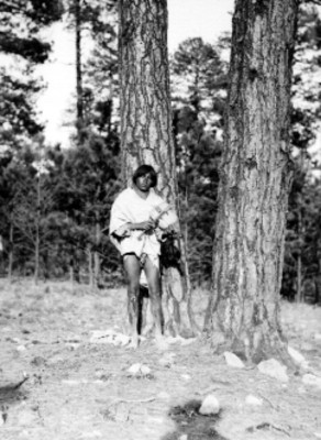 Tarahumara tocando violín recargado en un árbol de un bosque en Chihuahua