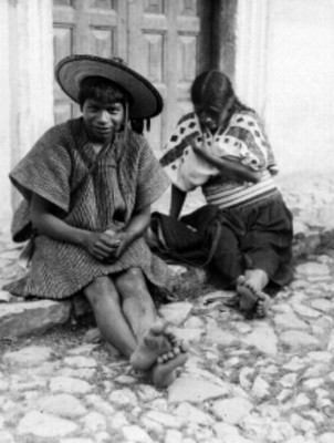 Pareja de zinacantecos zotziles centados frente a un edificio en un poblado de los Altos de Chiapas