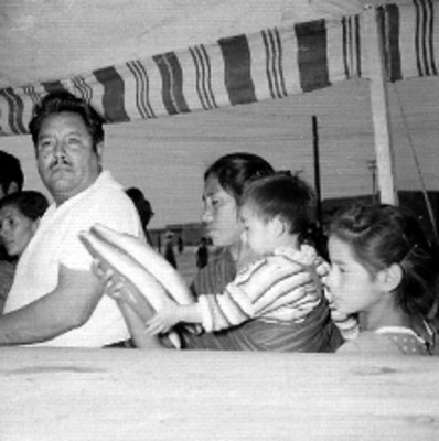 Mujer con niña en brazos en una tienda provisional durante la venta popular navideña de C.E.I.M.S.A, retrato