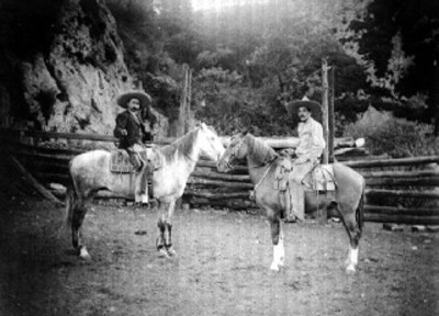 Charros posan sobre caballos uno frente al otro en zona boscosa