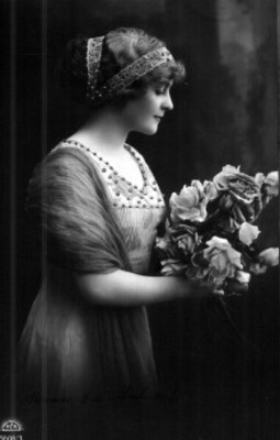 Mujer de perfil posa con vestido y adornos en el cabello, toma un racimo de flores entre sus manos