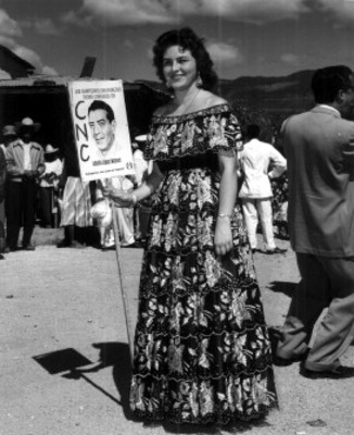 Mujer con traje folclórico sostiene propaganda electoral del candidato Adolfo López Mateos