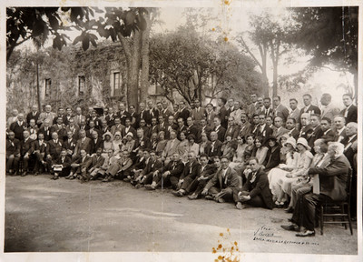 Funcionarios con condecoraciones acompañados por mujeres en un jardín, retrato de grupo