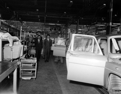 Hombres observan ensamblaje de automóviles en planta automotríz