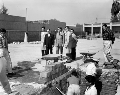 Hombres observan a albañiles durante construcción en escuela