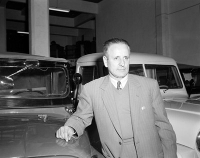 Ejecutivo de pie junto a automóviles en una agencia automotríz, retrato