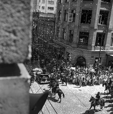 Adolfo López Mateos desfilando, a bordo de un auto escoltado por caballería, en una calle de la ciudad de México, toma en picada