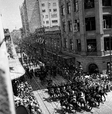Adolfo López Mateos saludando, a bordo de un auto escoltado por caballería, en una calle de la ciudad de México, toma en picada