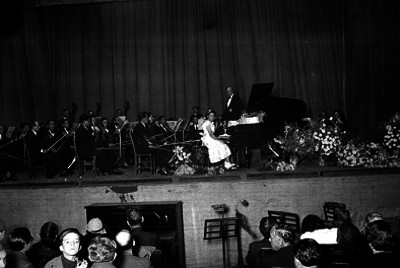 Pianista acompañada por una sinfónica en el escenario de un teatro
