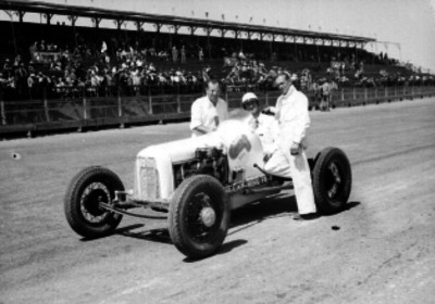 Piloto a bordo de su auto acompañado por dos hombres en la pista del autódromo Chapultepec