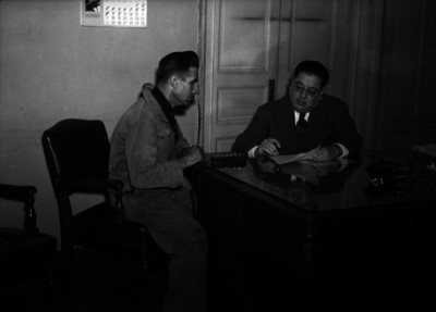 Funcionario público muestra documento a un hombre, dentro de oficina