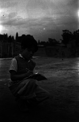 Niño sentado en vía pública anota en el cuaderno