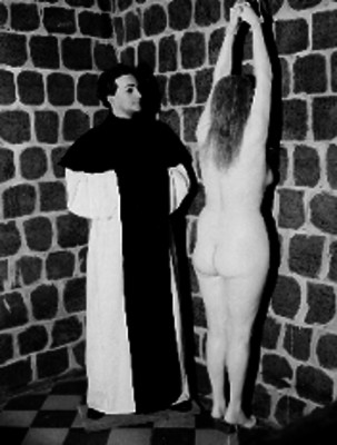 Figuras de cera de un fraile observando a una mujer desnuda con las manos amarradas