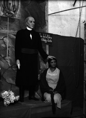 Miguel Hidalgo y Costilla posa su mano sobre la cabeza de una mujer, figuras de cera exhibidas en un museo