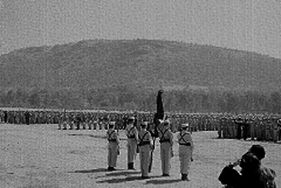 Contingente de soldados conscriptos rindiendo honores a la bandera en un campo militar