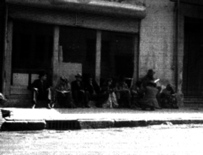 Grupo de gitanos sentados con unos caballeros en una banqueta afuera de unas oficinas