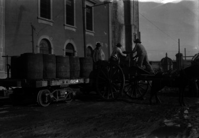 Hombres cargan barriles con pulque en una hacienda