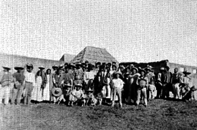 Personas de orígen campesino junto a una construcción grande, retrato