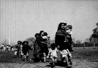 Mujeres con niños por un campo pastado, posiblemente saliendo de una posada