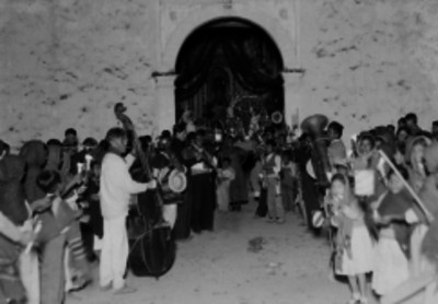 Hombres tocan instrumentos musicales y mujeres llevan en andas un nacimiento fuera de una iglesia