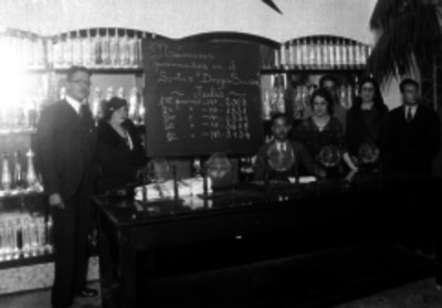 Hombres y mujeres vestidos elegante detrás de una mesa con esferas encima en un local de la Lotería Nacional, retrato