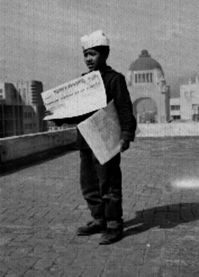 Joven voceador con periódicos en las manos observandose al fondo, el monumento a la revolución, retrato