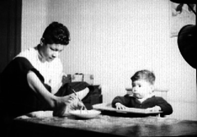 Niño manco comiendo con una parte de un brazo acompañado probablemente de su madre