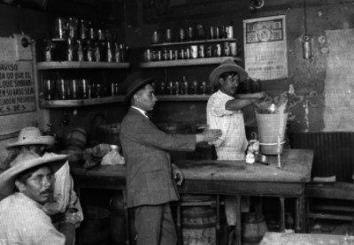 Pulquero despachando pulque a un hombre en el interior de una pulquería en la ciudad de México