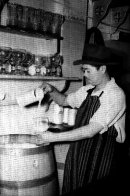 Pulquero sirviendo pulque de un barril a una copa en una pulquería