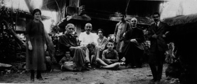 Familia humilde en compañía de un sacerdote, fuera de una casa