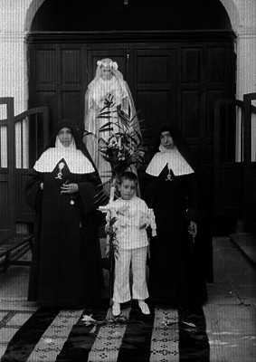 Niño acompañado de dos monjas durante su primera comunión en una iglesia, retrato de grupo