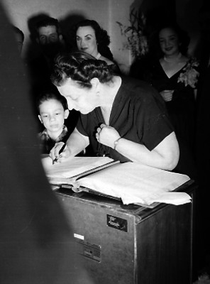Mujer firmando un libro como testigo de un matrimonio civil en una habitación