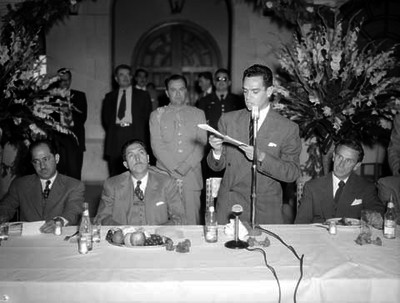 MIguel Alemán escuchando a un hombre pronunciar su discurso