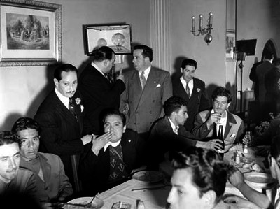 Luis Buñuel conversando con productores de cine durante una cena ofrecida a Miguel Alemán Valdés en un salón