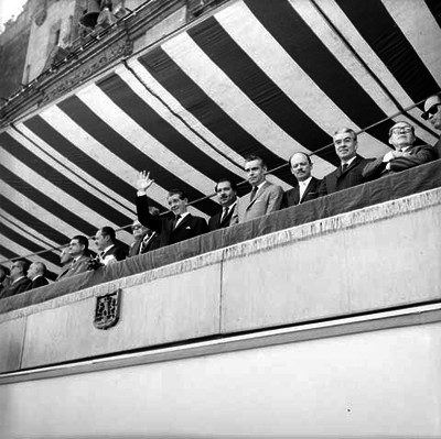 Adolfo López Mateos y su comitiva saludando desde un balcón, a los participantes de un desfile