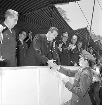 Adolfo López Mateos entregando una charola a un militar participante en el concurso ecuestre del cuerpo militar en un campo