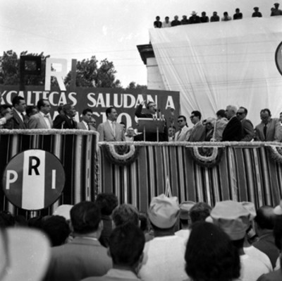 Adolfo López Mateos pronunciando un discurso en un presídium durante su campaña electoral por Tlaxcala, toma en contrapicada