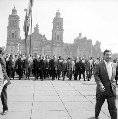Adolfo López Mateos izando la bandera nacional en el zócalo de la ciudad de México, acompañado por miembros de su gabinete